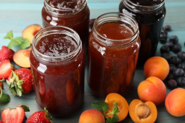 Kavanozlardaki farklı reçeller ve mavi ahşap masa üzerindeki malzemeler, yakın plan.