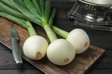 Taze taze soğanlar, kesme tahtası ve bıçakla siyah ahşap masa, yakın plan.