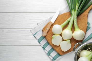 Taze taze taze soğanlar, tahta kesme tahtası ve beyaz ahşap masa üzerinde bıçak, düz yatış. Metin için boşluk