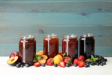 Kavanozlardaki farklı reçeller ve beyaz masadaki malzemeler. Metin için boşluk