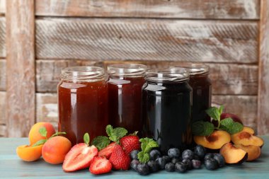 Kavanozlardaki farklı reçeller ve mavi ahşap masadaki malzemeler. Metin için boşluk