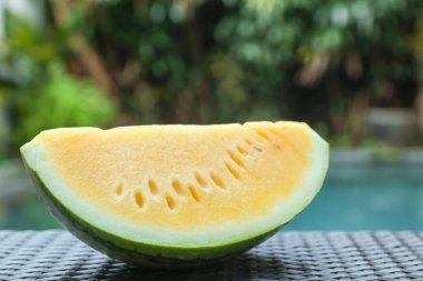 Açık havuz kenarında hasır masada lezzetli bir karpuz dilimi, yakın plan.