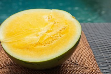 Olgun sarı karpuzun yarısı hasır masada, yüzme havuzunun yanında, yakın plan.