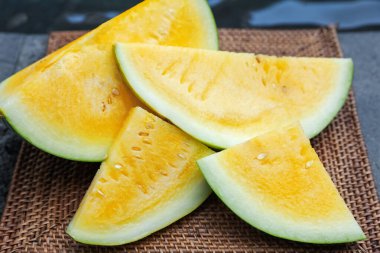 Yüzme havuzunun yanındaki masada olgun sarı karpuz parçaları, yakın plan.