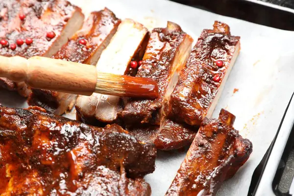 Fırçayla sosu pişirme tepsisindeki kaburgaların üzerine serpiştiriyorum.