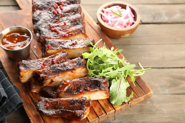 Lezzetli domuz pirzolası, roka, sos ve soğan ahşap masada, yakın plan.