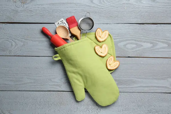 Farklı mutfak aletleri fırın eldiveni ve açık gri ahşap masa üzerinde avuç içi kurabiyeler.