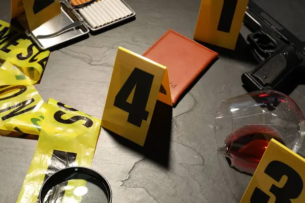 Adli tıp uzmanlığı. Gri arka planda delil, işaret ve polis bandı olan olay yeri, yakın plan.