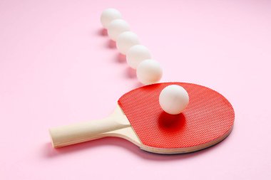 Pembe arka planda pinpon raketi ve toplar, yakın plan.