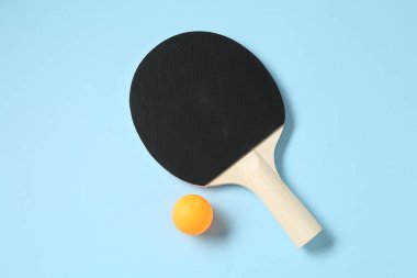 Masa tenisi raketi ve top açık mavi arkaplanda, düz yatıyordu.