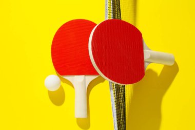 Ping pong raketleri, top ve ağ sarı arka planda, düz yatıyordu