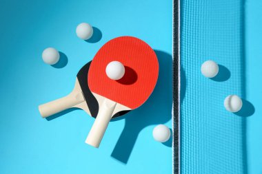 Masa tenisi raketleri, toplar ve net açık mavi arka planda, düz yatıyordu.