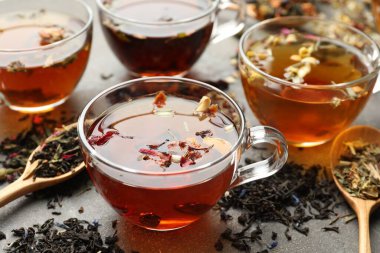 Cam fincanlarda aromatik bitki çayı ve gri masada kuru yapraklar, yakın plan.