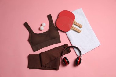 Spor kıyafetleri, masa tenisi raketleri, toplar, pembe arka planda havlu ve kulaklıklar, düz yatış.