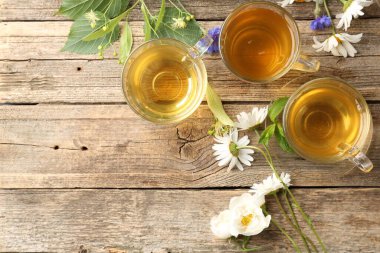 Cam fincanlarda aromatik bitki çayı, çiçekler ve ahşap masada yeşil yapraklar, düz yatak. Metin için boşluk