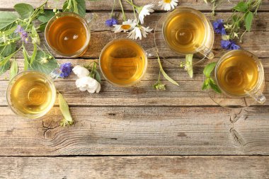 Cam fincanlarda aromatik bitki çayı, çiçekler ve ahşap masada yeşil yapraklar, düz yatak. Metin için boşluk