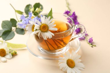 Cam fincanda aromatik bitki çayı ve bej arka planda farklı çiçekler, yakın plan.