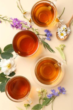 Cam fincanlarda aromatik bitki çayı ve bej arka planda farklı çiçekler.