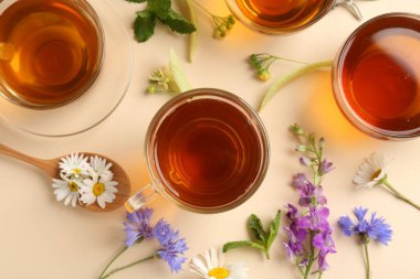 Cam fincanlarda aromatik bitki çayı ve bej arka planda farklı çiçekler.