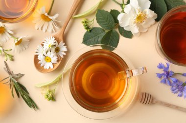 Cam fincanlarda aromatik bitki çayı ve bej arka planda farklı çiçekler.