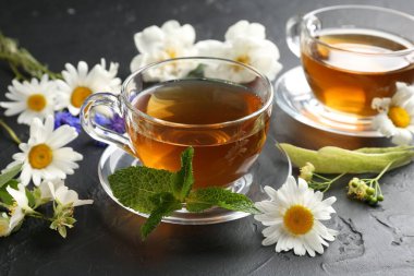 Cam bardaklarda romatik bitki çayı, farklı çiçekler ve siyah masada nane şekeri, yakın plan.