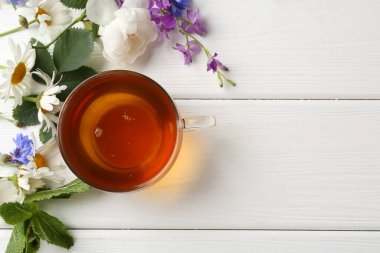 Cam fincanda aromatik bitki çayı, farklı çiçekler ve beyaz ahşap masada nane şekeri. Metin için boşluk