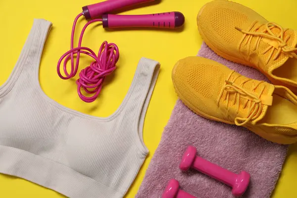 Spor kıyafetleri, atlama halatı, dambıllar, havlu ve spor ayakkabıları sarı arka planda, düz yatıyordu.