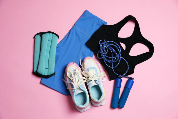 Sportswear, ankle weights, skipping rope and sneakers on pink background, flat lay