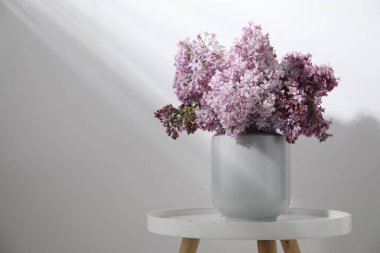 Beyaz duvarın yanındaki masada vazodaki güzel leylak çiçekleri, metin için yer var.