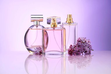 Ayna yüzeyinde mor arkaplana karşı parfüm şişeleri ve leylak çiçekleri