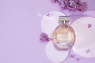 Bir şişe parfüm ve açık mor arka planda güzel leylak çiçekleri. Metin için boşluk