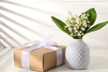 Vadi çiçeklerinin güzel zambakları ve beyaz masada hediye. Metin için boşluk