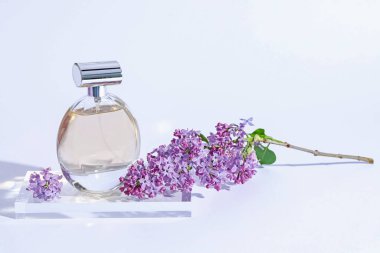 Parfüm şişesi ve dalında açık gri arka planda leylak çiçekleri, yakın plan.