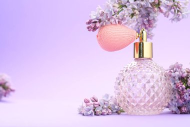 Parfüm şişesi ve mor arkaplanda leylak çiçekleri, yakın plan. Metin için boşluk
