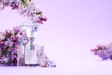 Parfüm şişesi ve mor arkaplanda leylak çiçekleri, yakın plan. Metin için boşluk