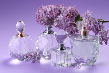 Parfüm şişeleri ve mor arkaplanda leylak çiçekleri olan dallar, yakın plan.