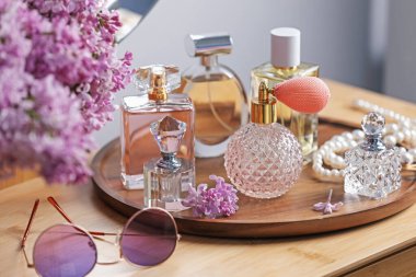 Parfüm şişeleri, aksesuarlar ve ahşap masada leylak çiçekleri.