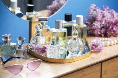 Parfüm şişeleri, aksesuarlar ve ahşap masada leylak çiçekleri.