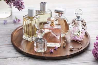 Beyaz ahşap masada, parfüm şişeleri ve leylak çiçekleri, yakın plan.