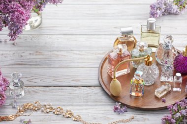 Beyaz ahşap masada parfüm şişeleri, aksesuarlar ve leylak çiçekleri. Metin için boşluk