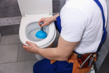 Tesisatçı tuvalet tıkanıklığını açıyor, içeride pompa var, yakın plan.