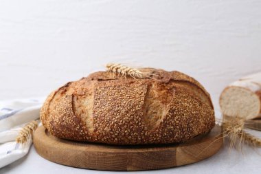 Taze pişmiş ekmek, susam tohumları ve gri masanın üzerindeki çiviler, arka planda ışığa karşı, yakın plan.