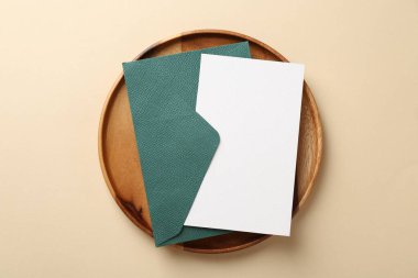 Boş davetiye kartı, zarf ve bej arka planda ahşap tepsi, üst görünüm