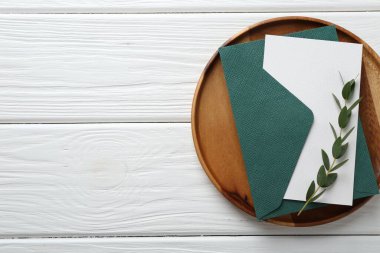 Boş davetiye kartı, zarf, tepsi ve dal beyaz ahşap masa, üst manzara. Metin için boşluk