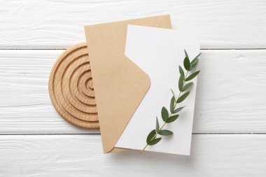 Boş davetiye kartı, zarf ve dal beyaz ahşap masa, üst görünüm