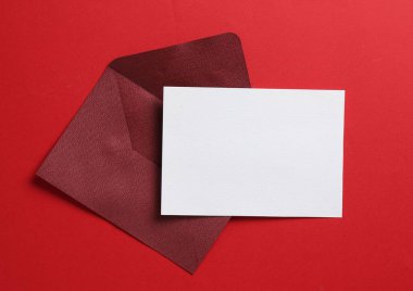 Kırmızı arka planda boş davetiye ve zarf, üst manzara. Tasarım için boşluk