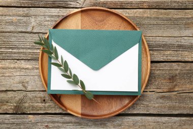 Boş davetiye kartı, zarf ve yeşil dal, ahşap masa, üst manzara.