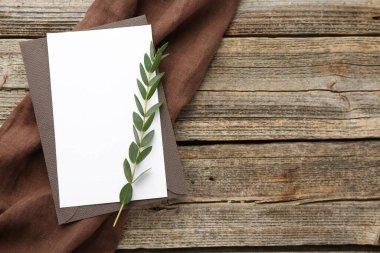 Boş davetiye kartı, zarf ve ahşap masanın üzerinde yeşil dal, üst manzara. Metin için boşluk