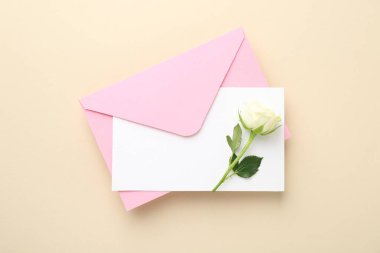 Boş davetiye kartı, bej arka planda zarf ve çiçek, üst görünüm