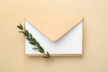 Boş davetiye kartı, zarf ve bej arka planda yeşil dal, üst görünüm